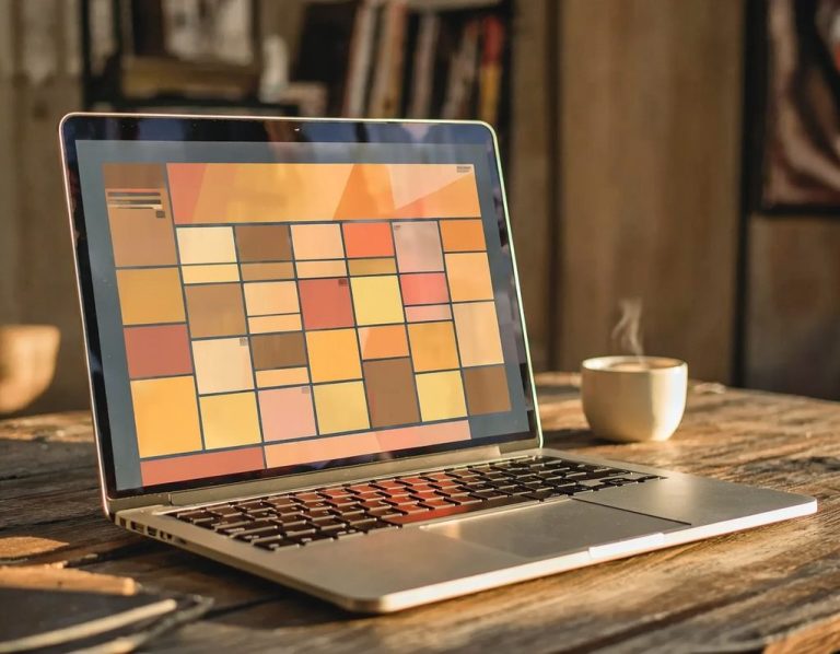 Laptop on a wooden table with a grid pattern on the screen and a steaming coffee cup.